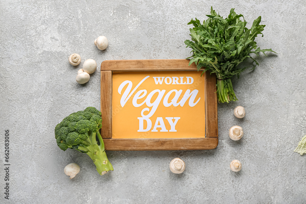 Board with text VEGAN DAY and different fresh vegetables on grey background