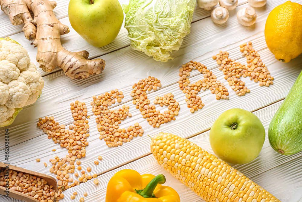 Word VEGAN made of dried peas and different fresh vegetables on white wooden background