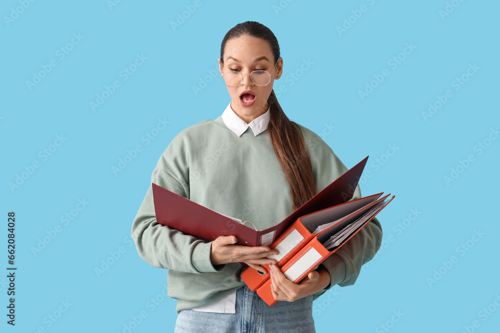 Shocked young woman with document folders on blue background