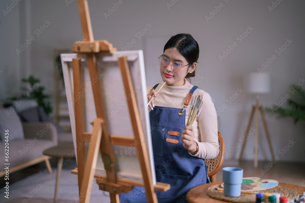 Young asian female artist sitting front of canvas and thinking idea to drawing and painting artwork