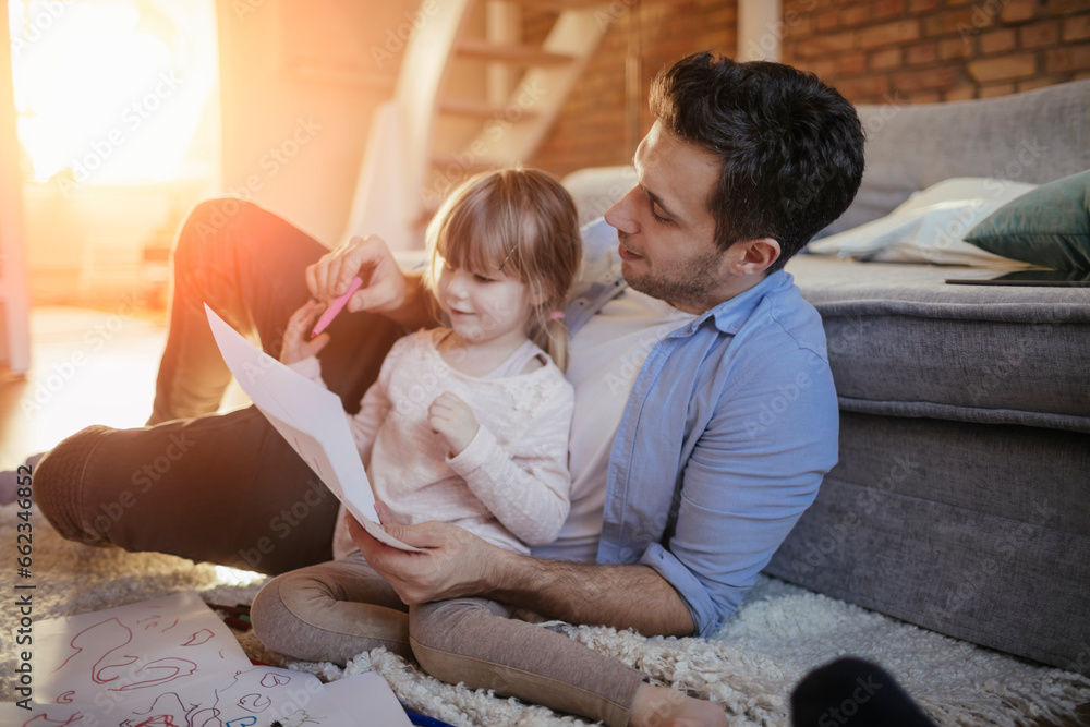 Young father drawing with his daughter on the floor in the living room