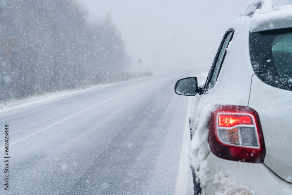 The car is driving on a winter road in a blizzard.