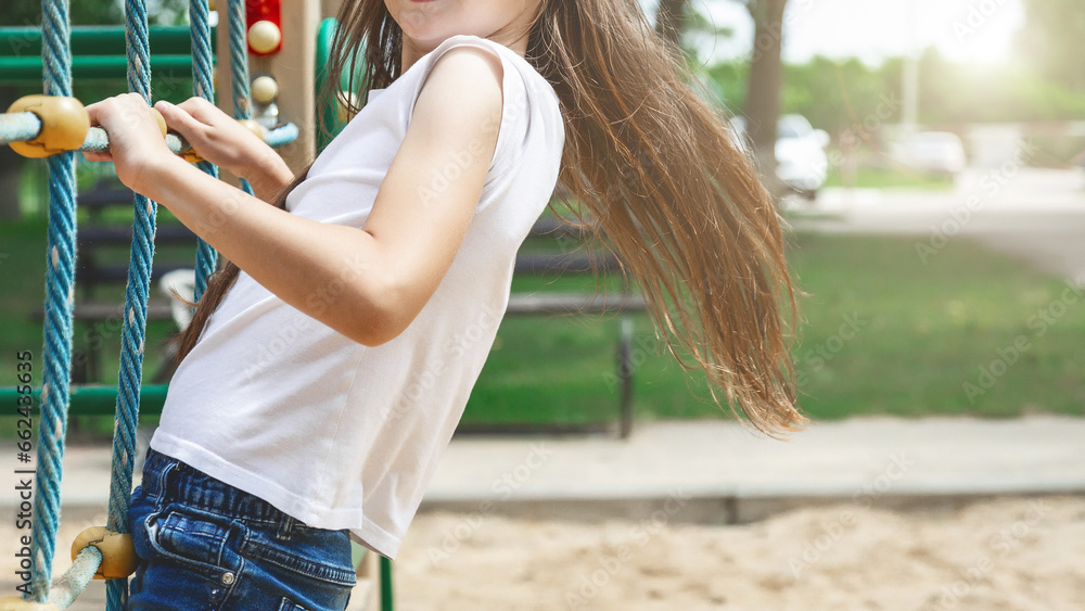 child girl holding rope while spending time on playground near blurred background of green park