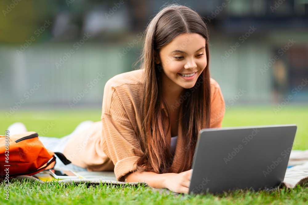 Happy woman student immersed in laptop work, quiet university campus