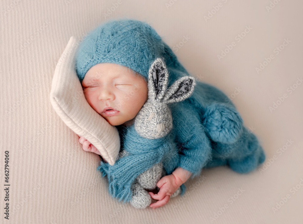 Adorable newborn baby boy sleeping with bunny toy wearing knitted hat and clothes. Cute infant child kid napping on pillow