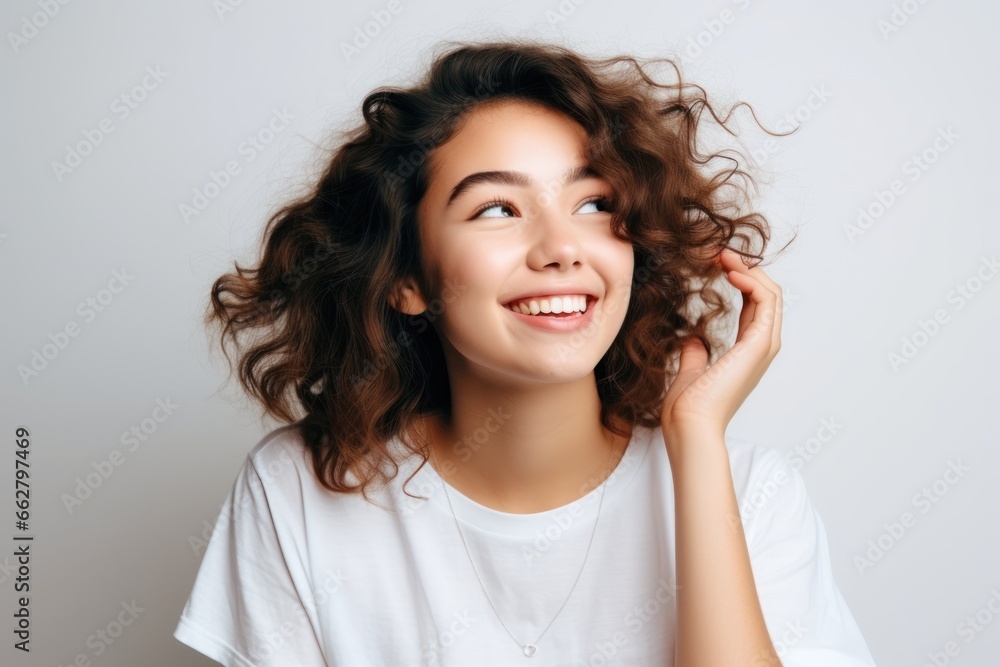 Beautiful young girl with curly hair in white t-shirt cheerfully smiling over grey background. Happiness. Human emotions