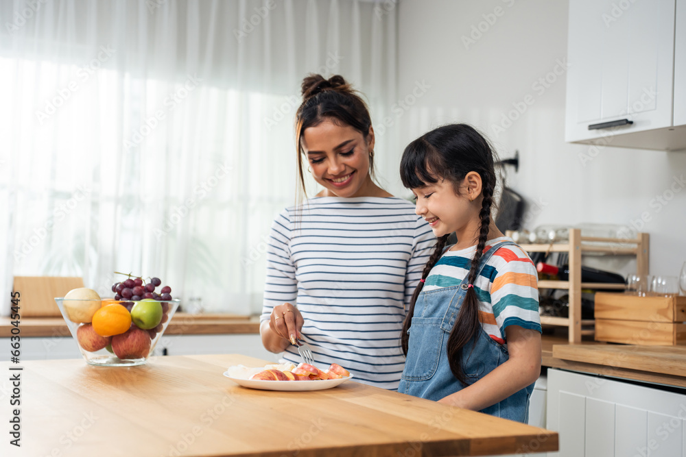 Caucasian little kid biting an apple with mother in kitchen room.