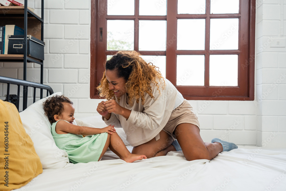 African loving mom play with cute baby girl child on bed in bedroom. 