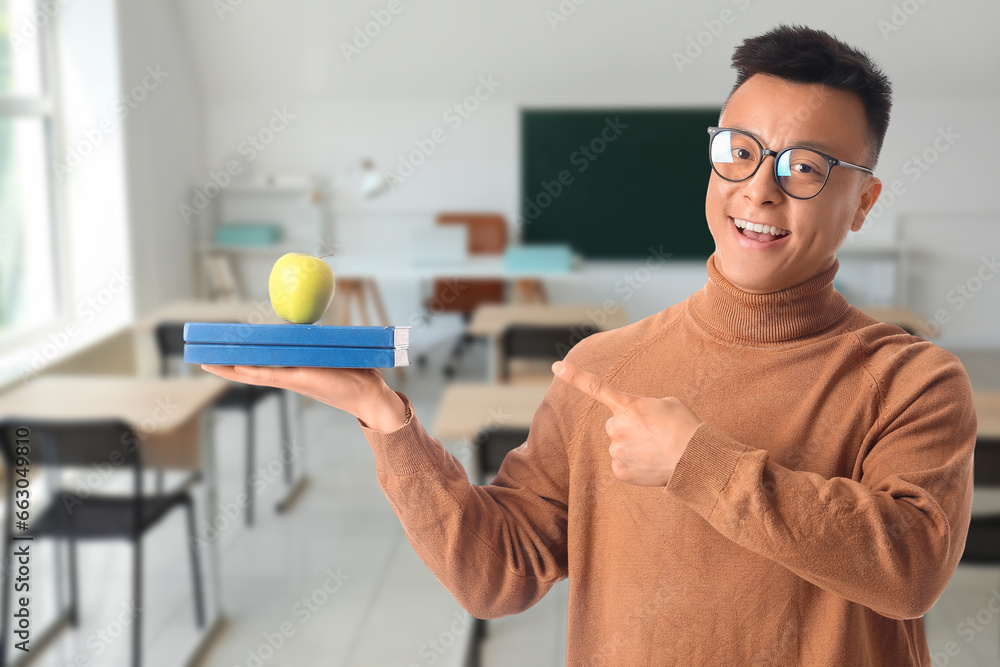 Portrait of male Asian teacher with apple and books in classroom