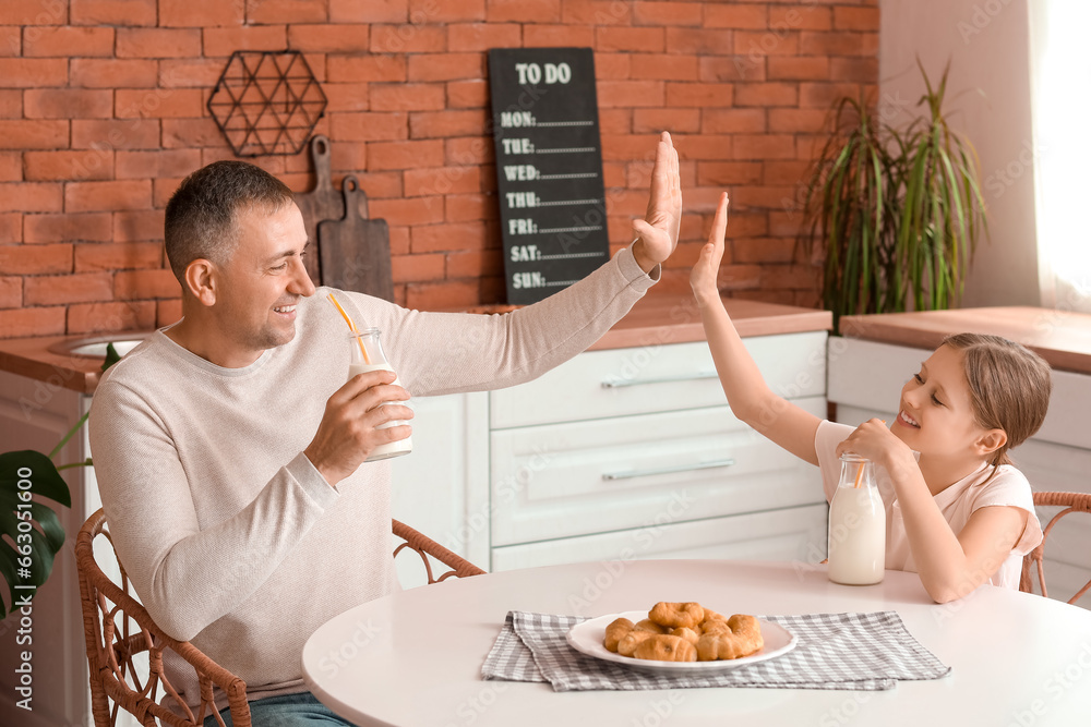 Little girl with her father drinking milk and giving each other high-five in kitchen