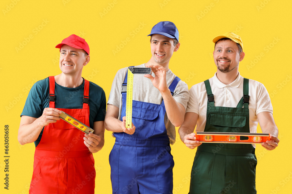 Team of male builders with levels on yellow background