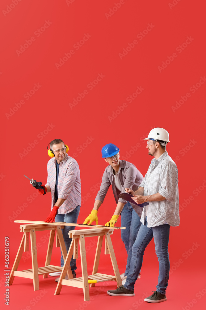 Team of male builders with tools on red background