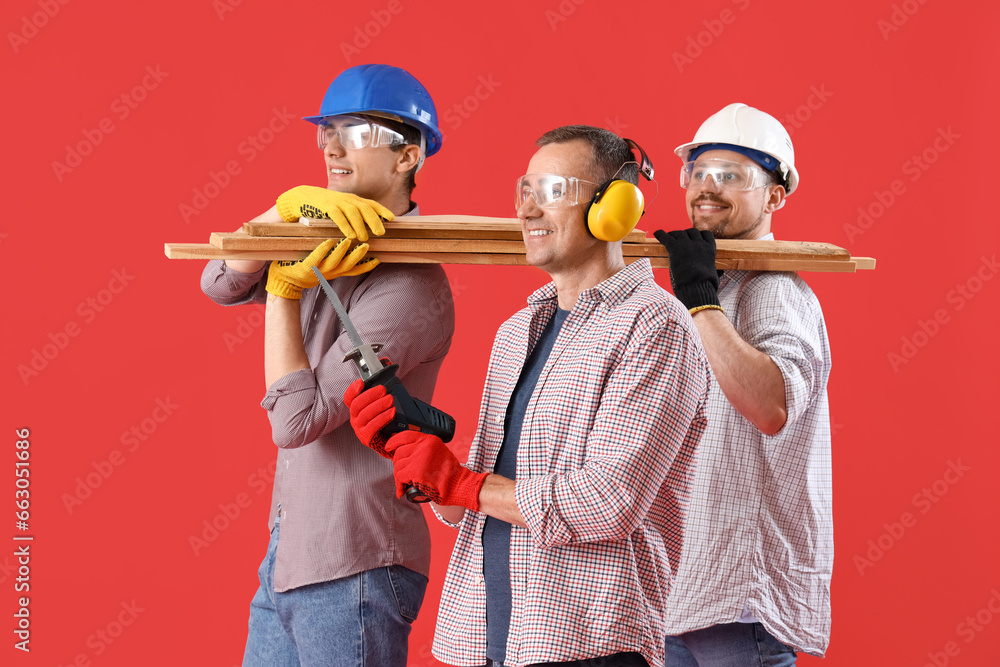 Team of male builders with wooden planks on red background