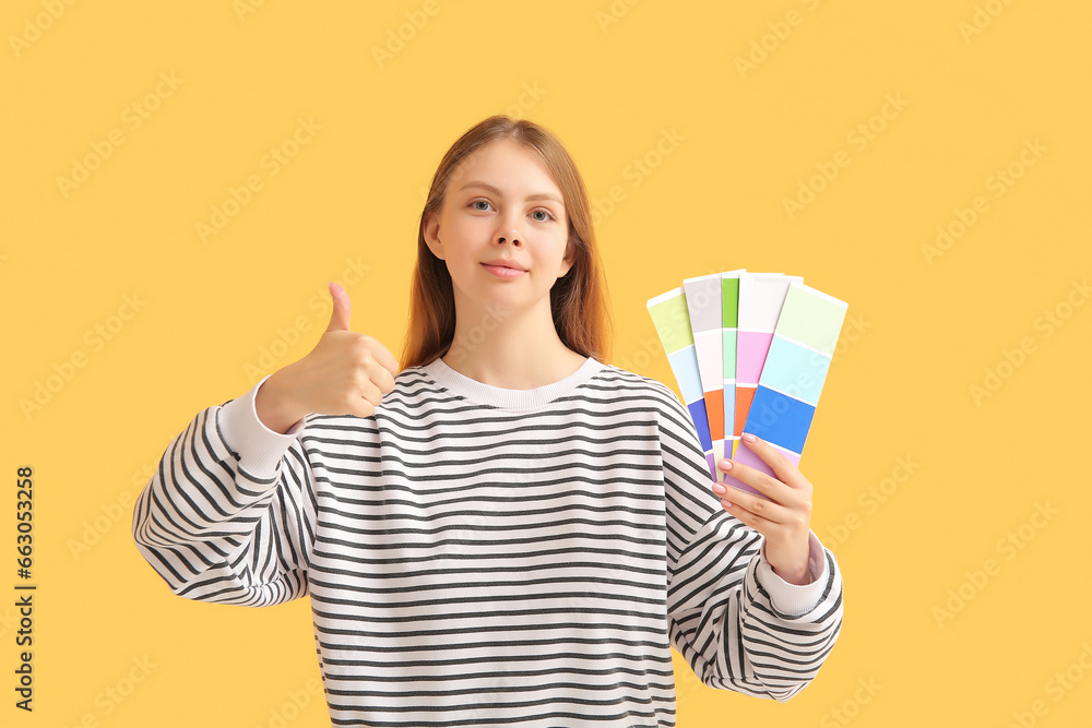 Young woman with color samples showing thumb-up on yellow background