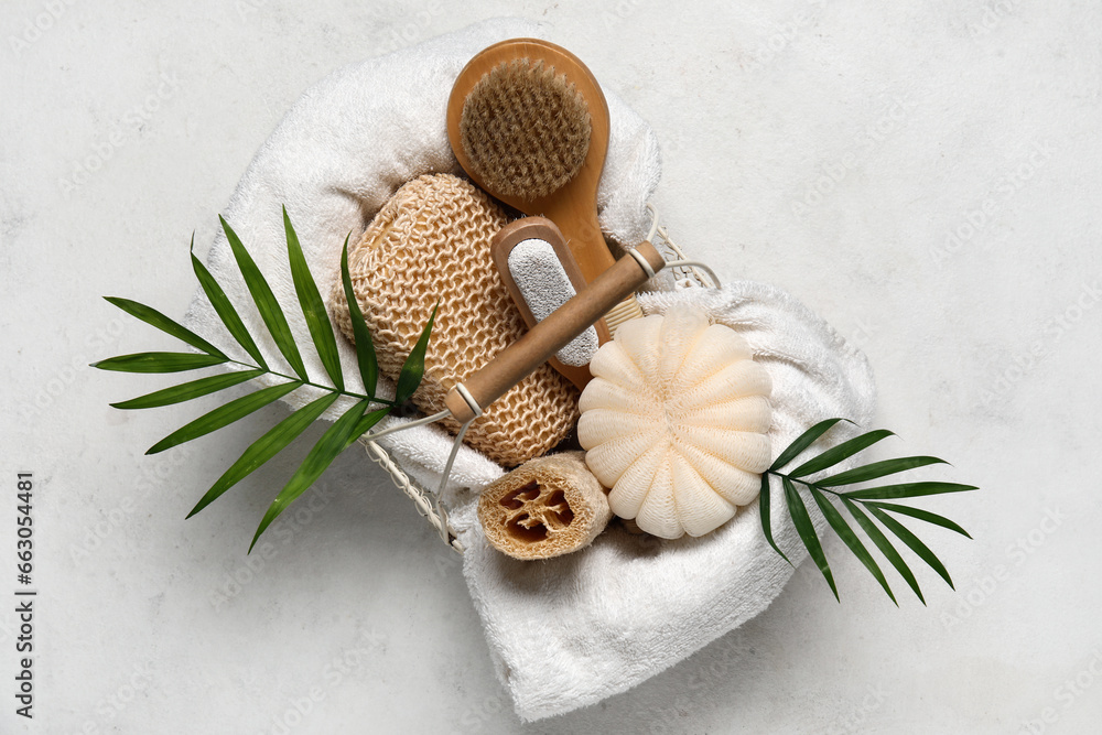 Basket with different bath supplies and palm leaves on light background