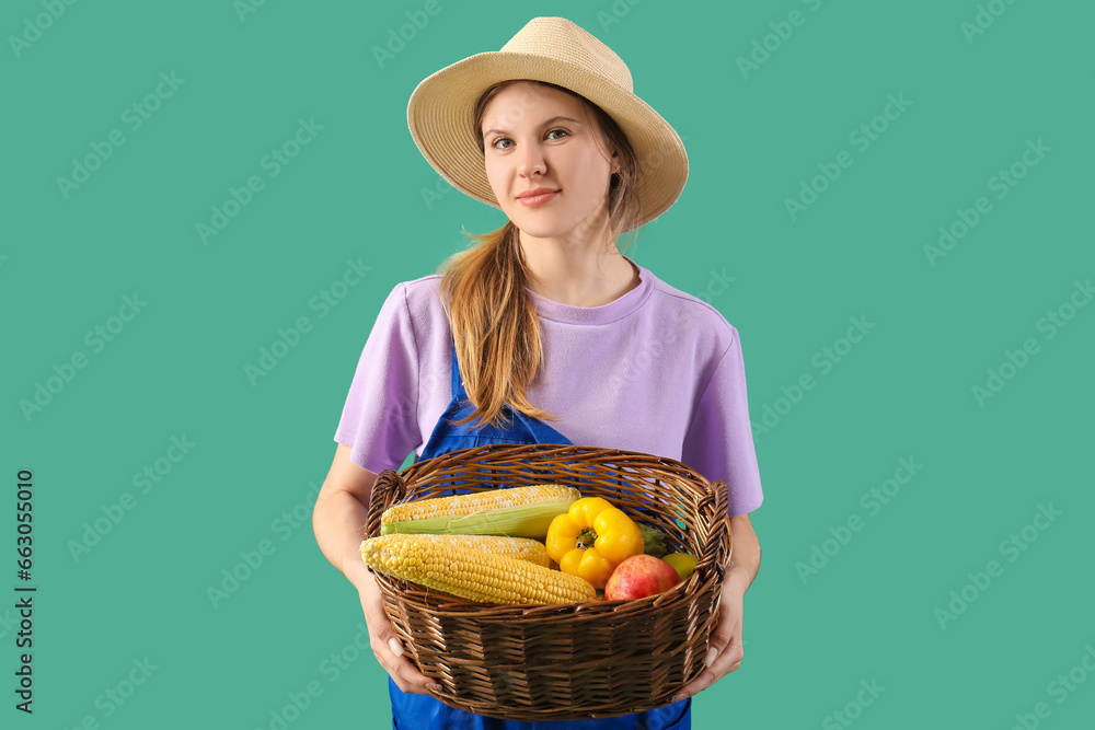 Beautiful young female farmer with wicker basket full of ripe vegetables and fruits on green background