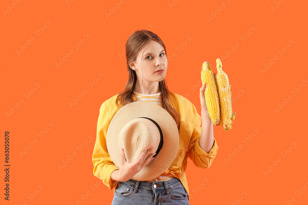 Beautiful young female farmer with ripe corn cobs on orange background