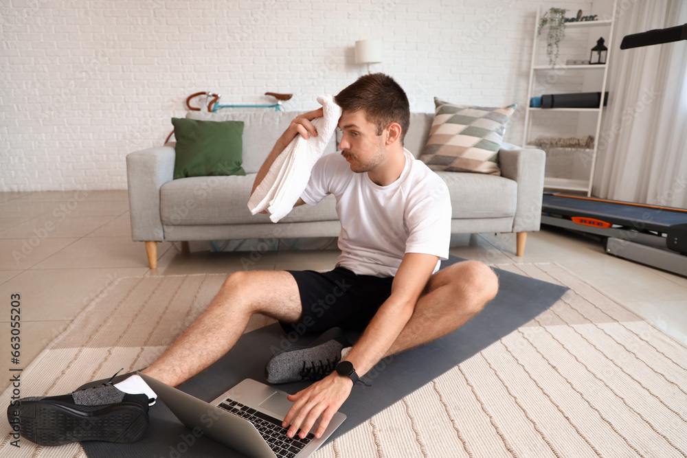 Sporty young man with laptop resting after training at home