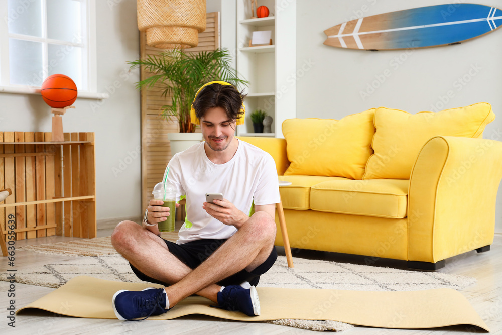 Sporty young man with healthy smoothie listening to music at home