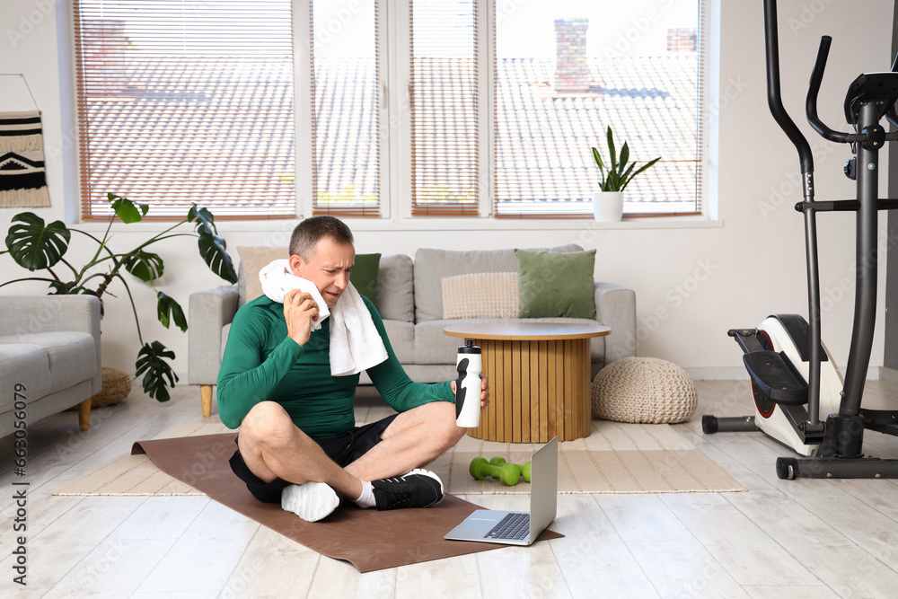 Sporty mature man with bottle of water after training at home