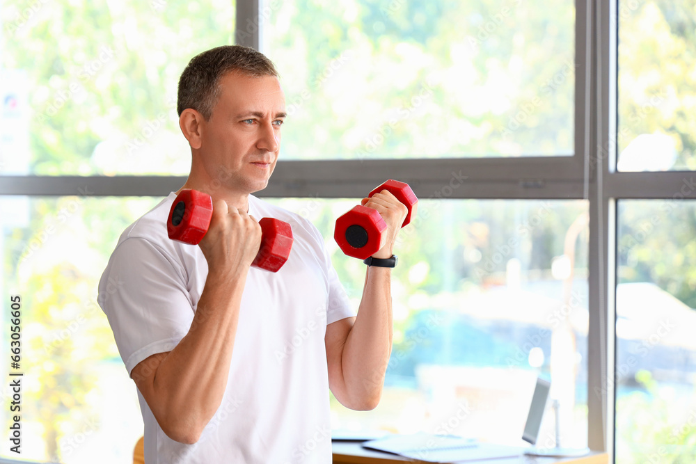 Sporty mature man training with dumbbells at home