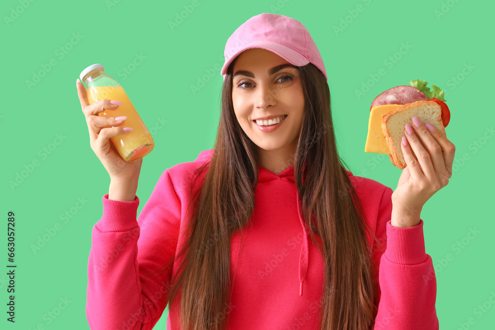 Young woman with tasty sandwich and bottle of juice on green background