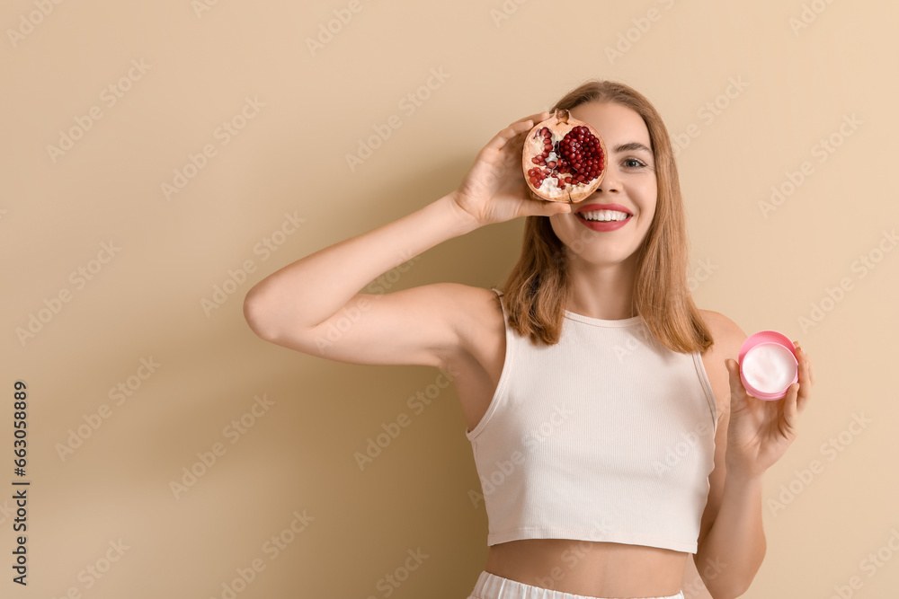 Young woman with pomegranate and jar of cream on beige background