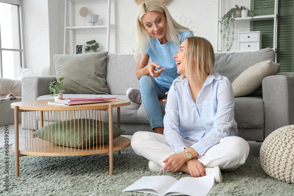 Happy young beautiful woman with her mother sitting in living room and reading magazines