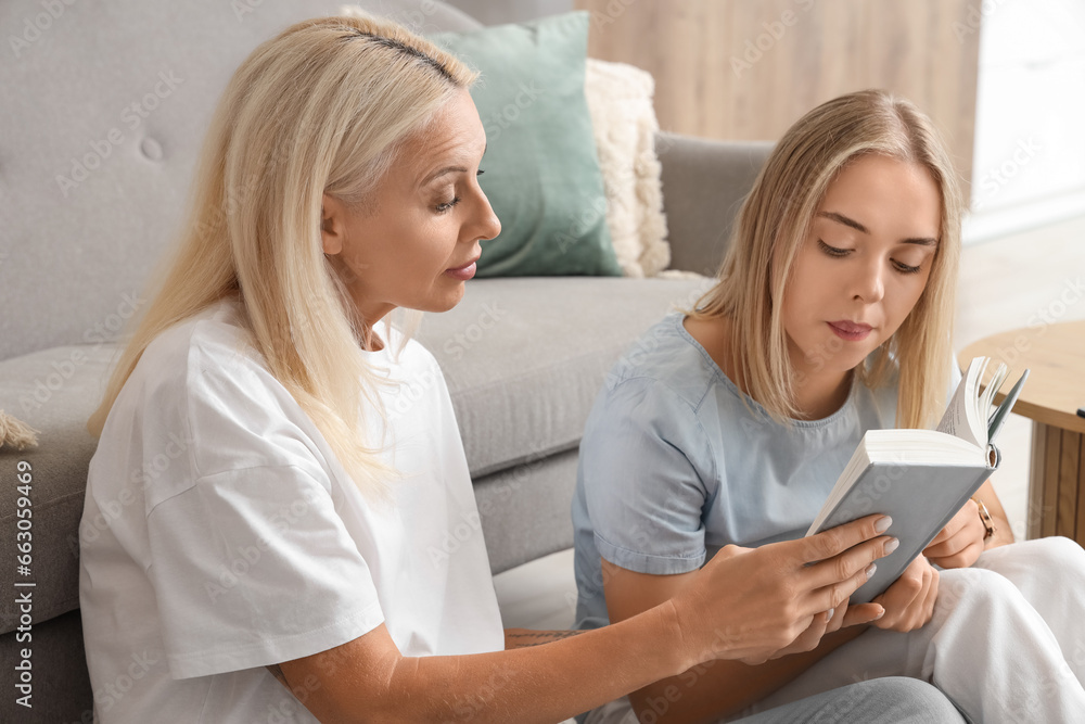 Young beautiful woman with her mother reading book together in living room