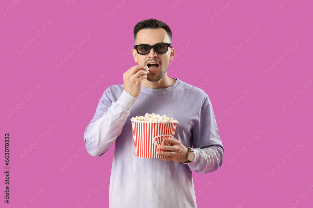 Happy young man in 3D glasses eating popcorn on purple background