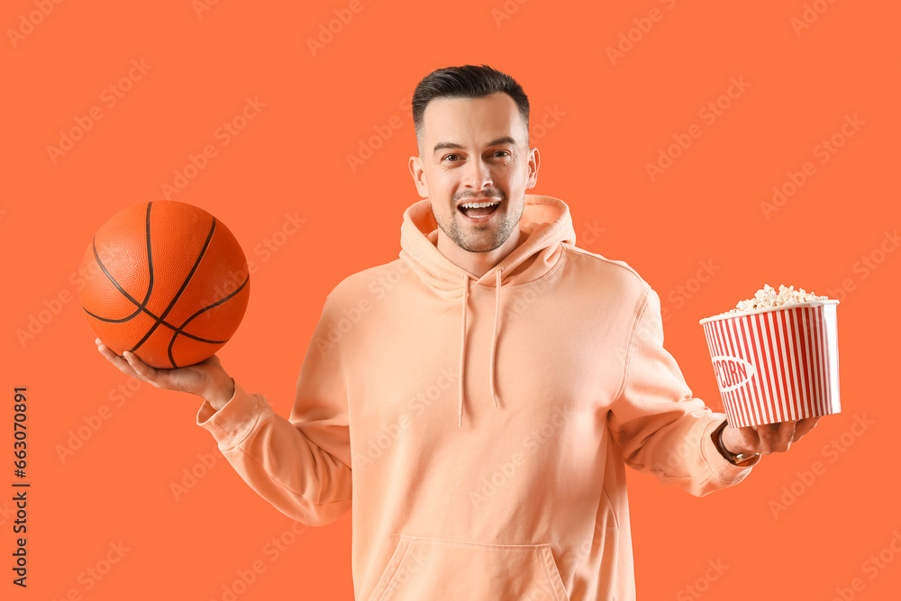 Happy young man with ball and popcorn on orange background