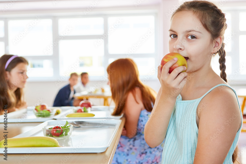 Girl eating fresh apple sitting in school cafeteria