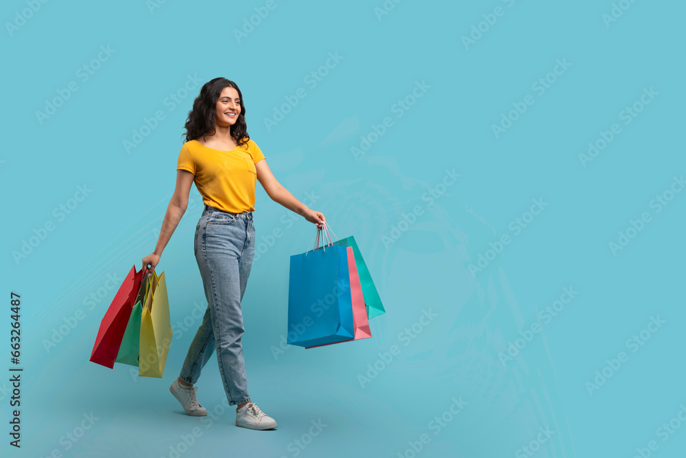 Positive young indian woman shopaholic walking with purchases