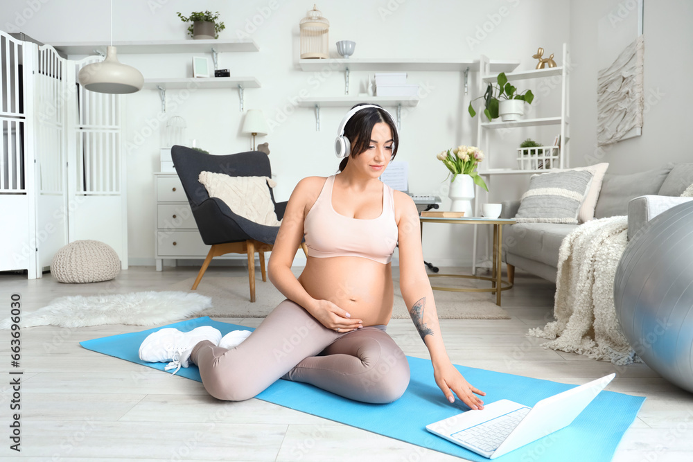 Sporty young pregnant woman in headphones using laptop at home