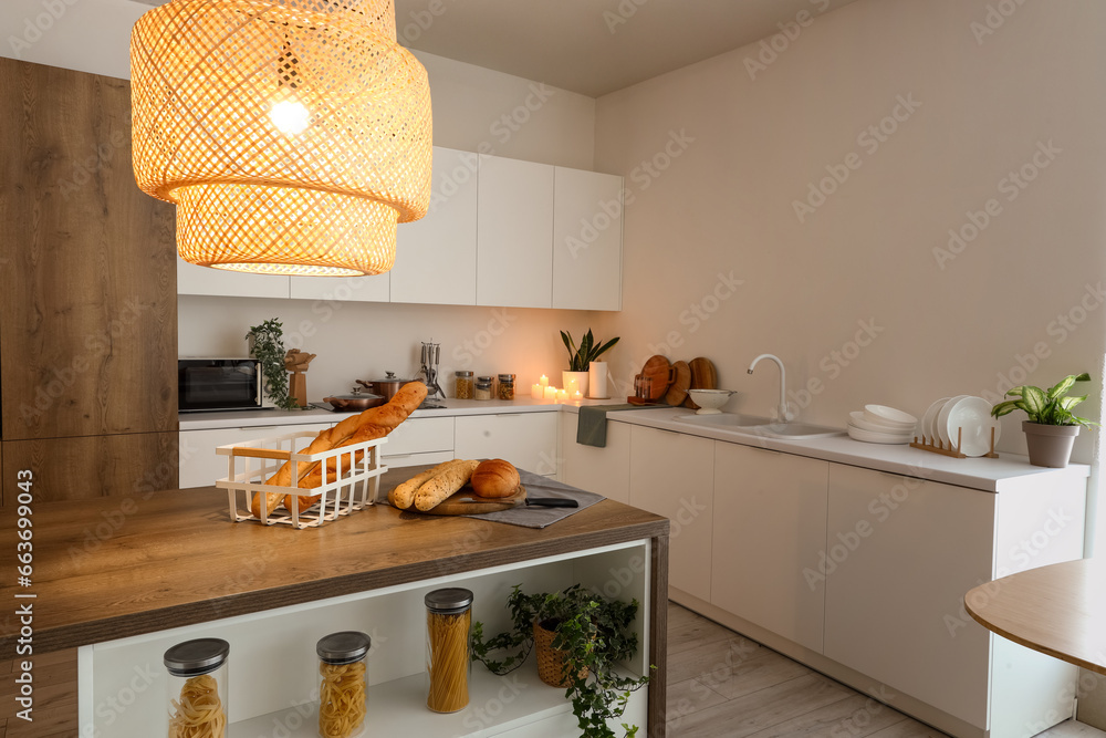 Interior of modern kitchen with island, glowing lamp and burning candles