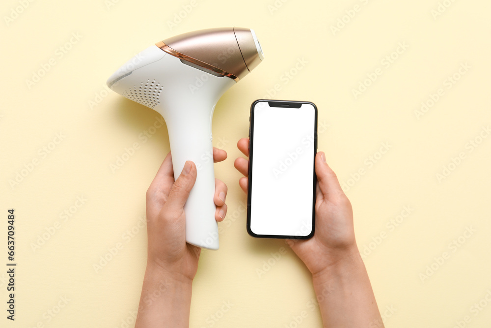 Female hands with mobile phone and modern photoepilator on beige background