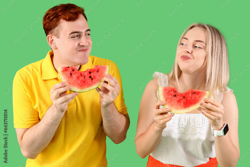 Young beautiful man and woman eating slices of fresh watermelon on green background