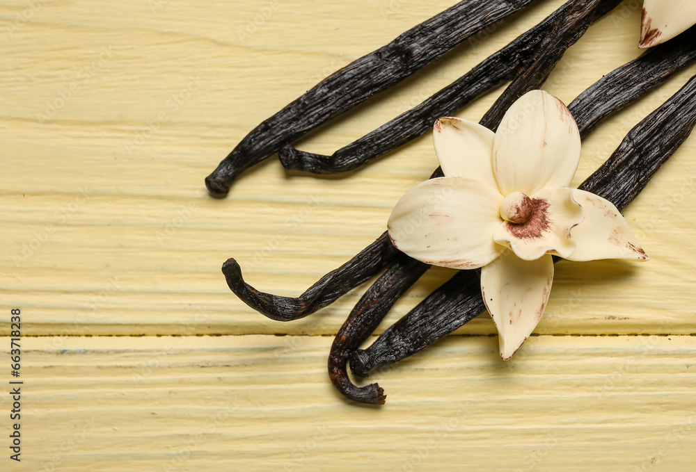 Aromatic vanilla sticks and flower on yellow wooden background