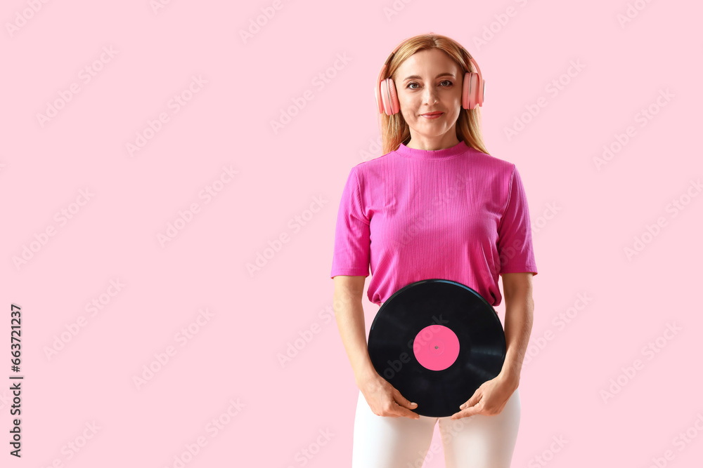 Stylish mature woman in headphones with vinyl disc on pink background