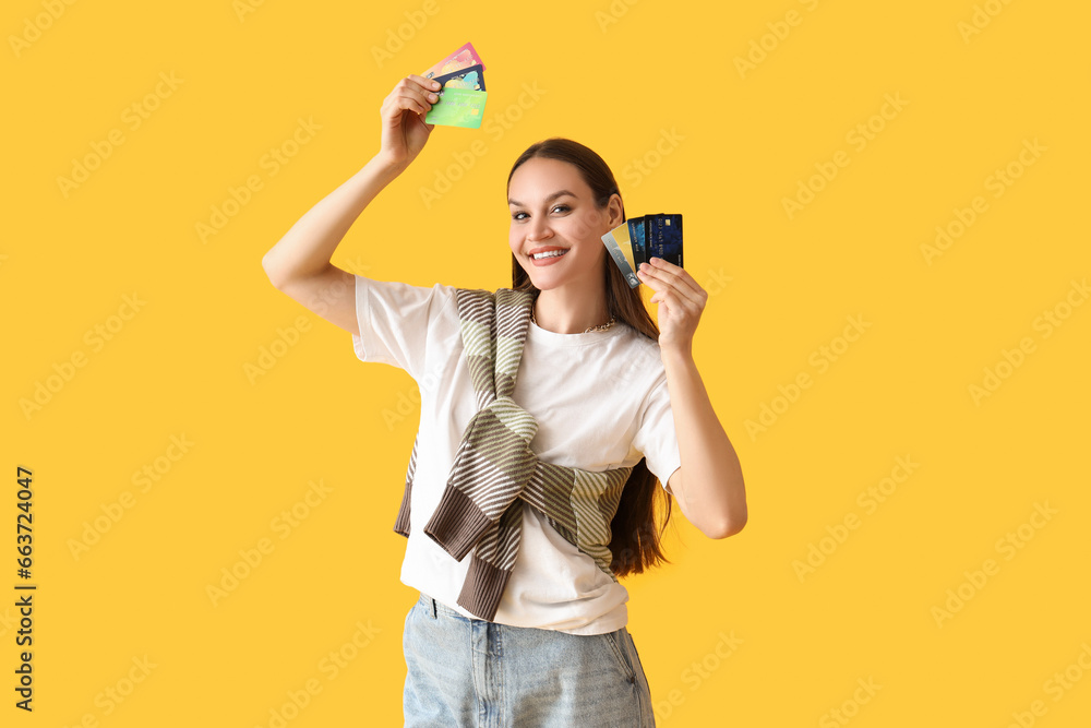 Young woman with credit cards on yellow background