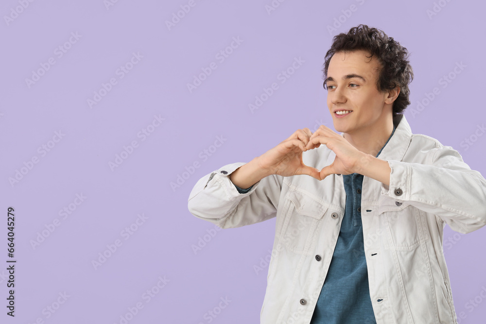 Young man making heart with his hands on lilac background