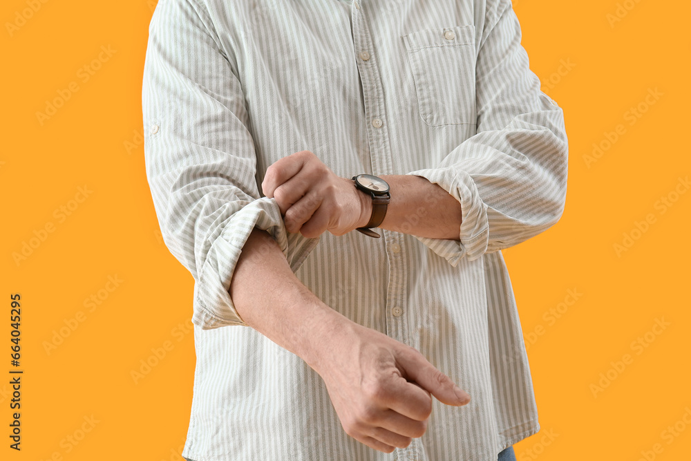 Mature man rolling up his sleeve on yellow background, closeup