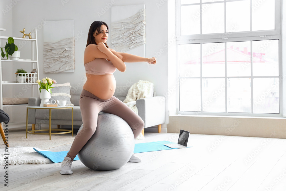 Sporty young pregnant woman training with fitball at home