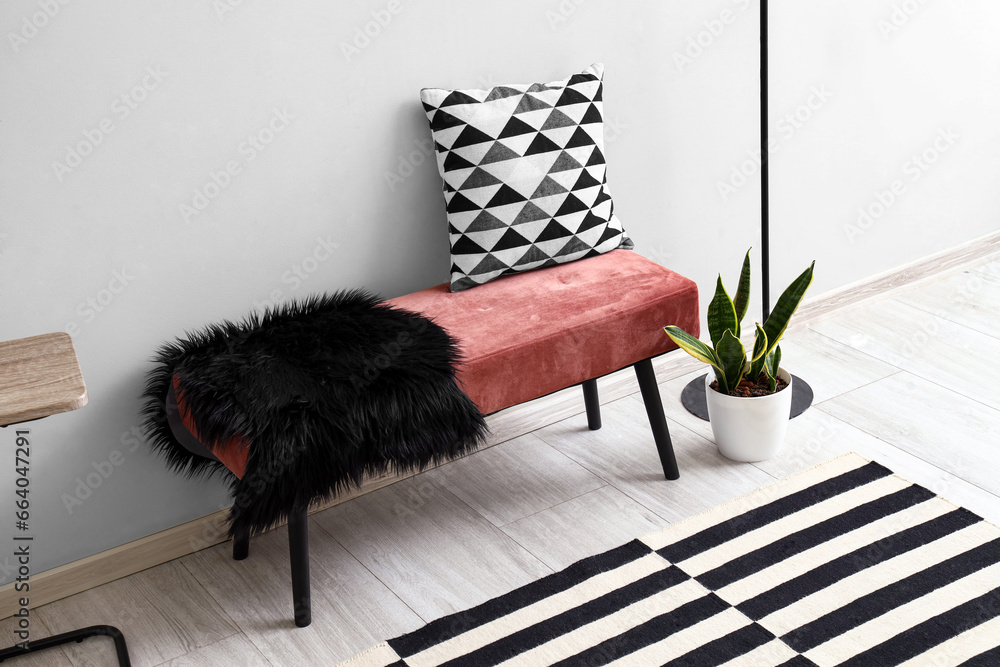 Pink bench with cushion, fur rug and houseplant near white wall