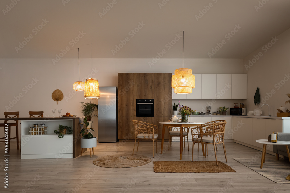 Interior of modern kitchen with dining table, island and glowing lamps