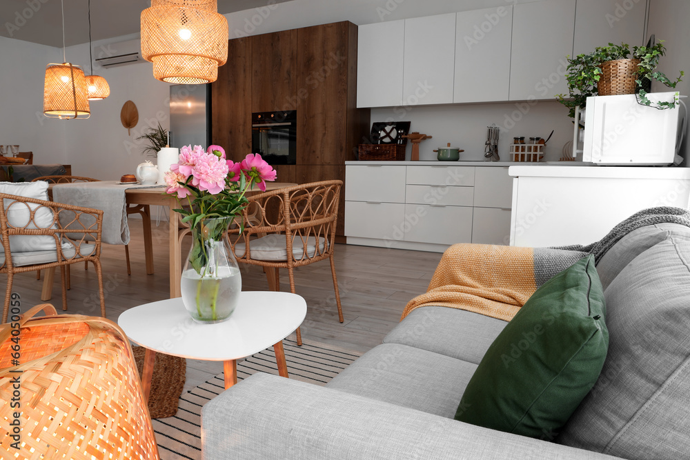 Vase with blooming peony flowers on coffee table in interior of modern open space kitchen