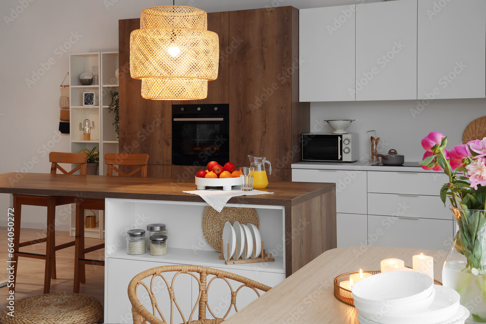 Interior of modern kitchen with dining table, island and glowing lamps