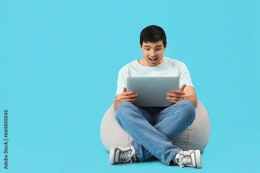 Surprised male programmer with laptop sitting on blue background