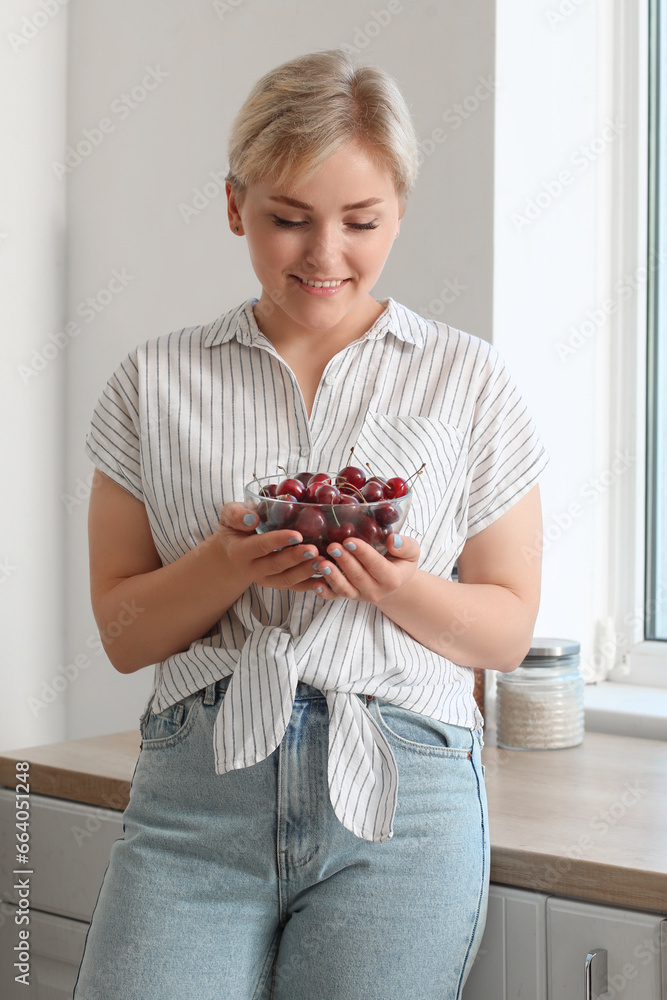 Beautiful young happy woman with bowl of ripe cherries in kitchen