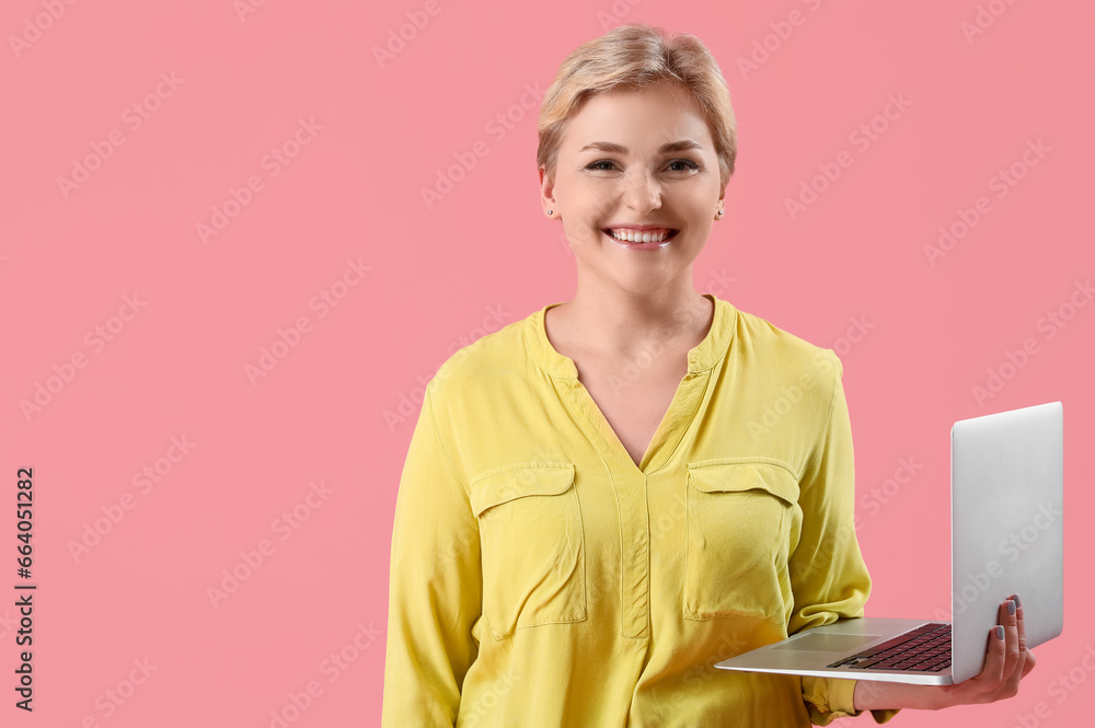 Happy young female programmer with laptop on pink background